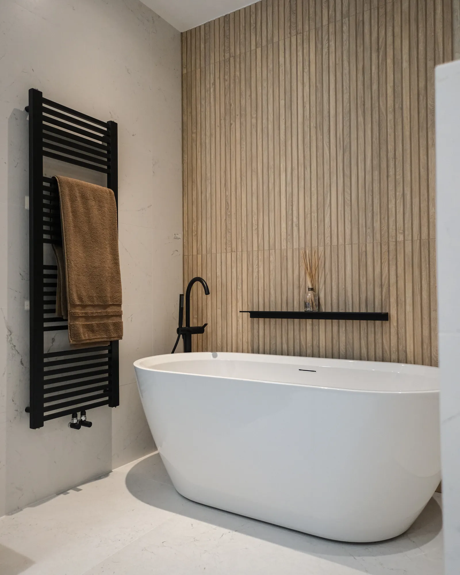 Vrijstaand bad met zwarte designradiator en houtlook wand